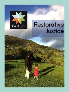 An older male-presenting person in a Colombian ruana is standing with a small female-presenting child as they look up a mountain at a rainbow in front of clouds. The words on the image say "Restorative Justice" and the Keduzi logo is there, which is a colourful flower.